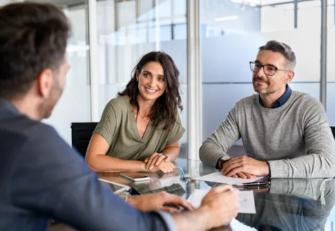 Mid adult woman with husband listening to businessman during meeting in conference room.